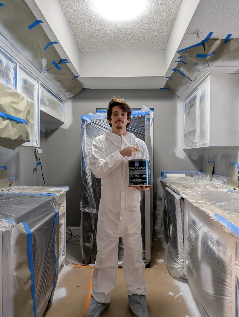 Painter holding a can of Sherwin-Williams Gallery Series topcoat in a masked kitchen