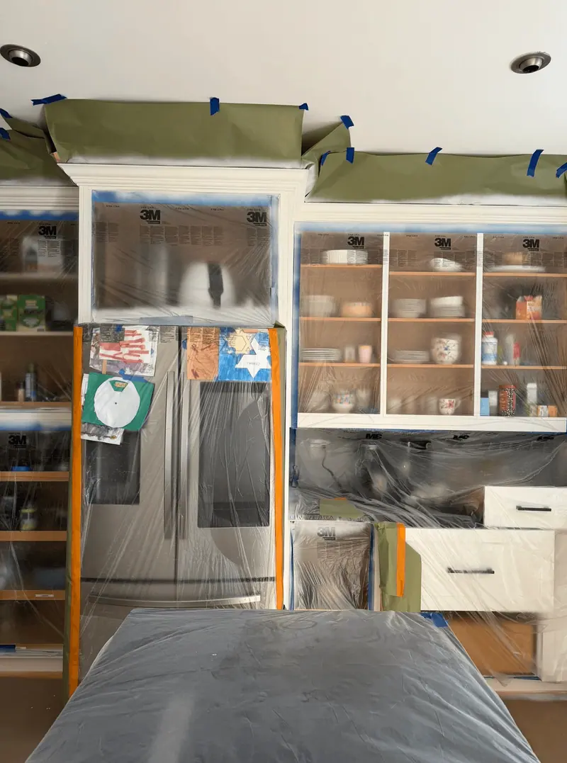 Cabinets and refrigerator masked with tape and plastic during spraying