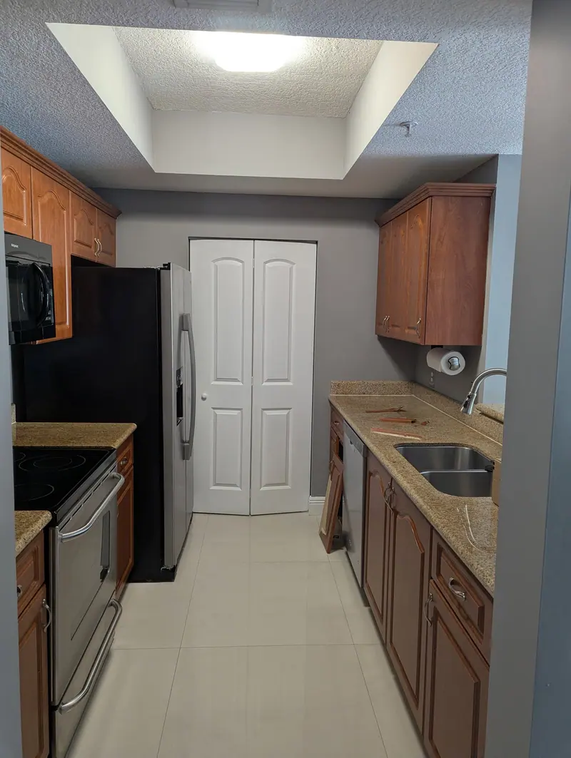 Coral Gables galley kitchen before painting, wood-grain cabinets with granite countertops