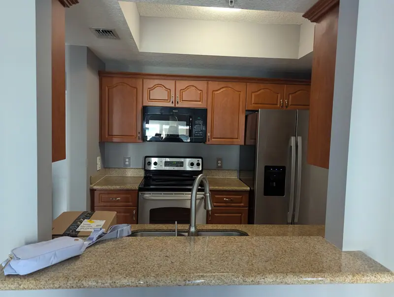 Coral Gables kitchen before painting, wood-grain cabinets around the range and refrigerator