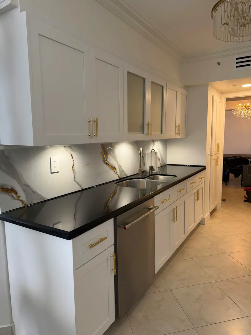 White upper and lower cabinets along a black countertop with under-cabinet lighting, Sunny Isles Beach